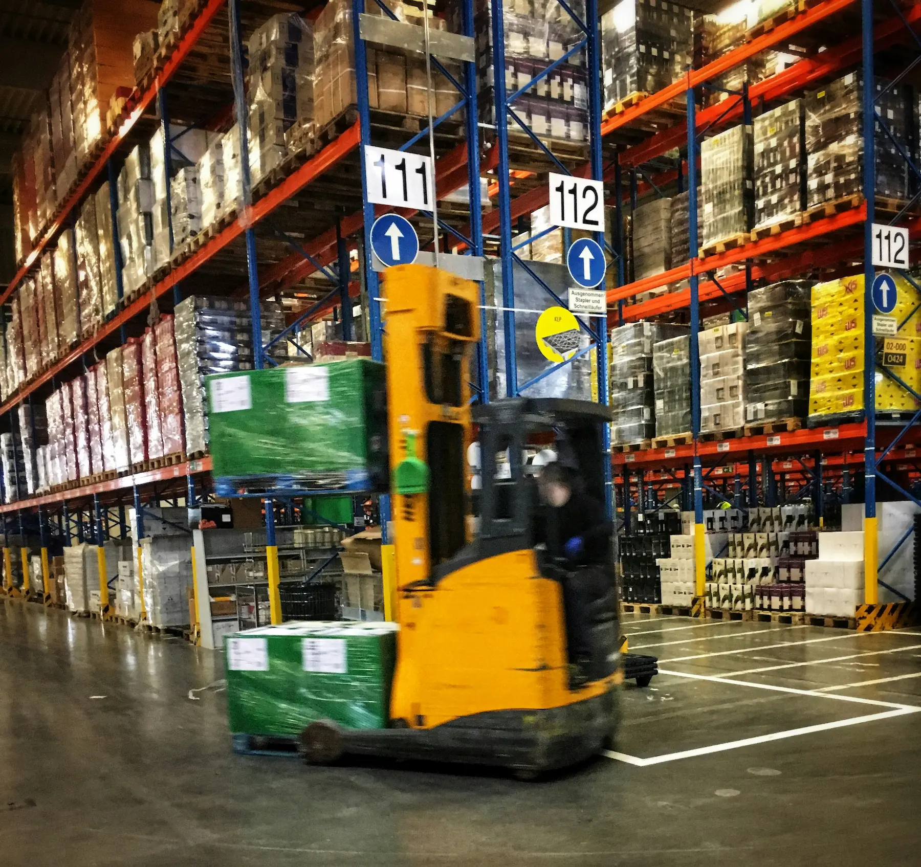 A forklift driving through a warehouse filled with pallets